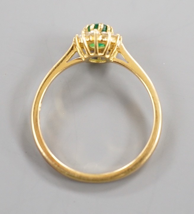 A modern 18ct gold, oval cut emerald and diamond chip set oval cluster ring, size N/O, gross weight 2.5 grams